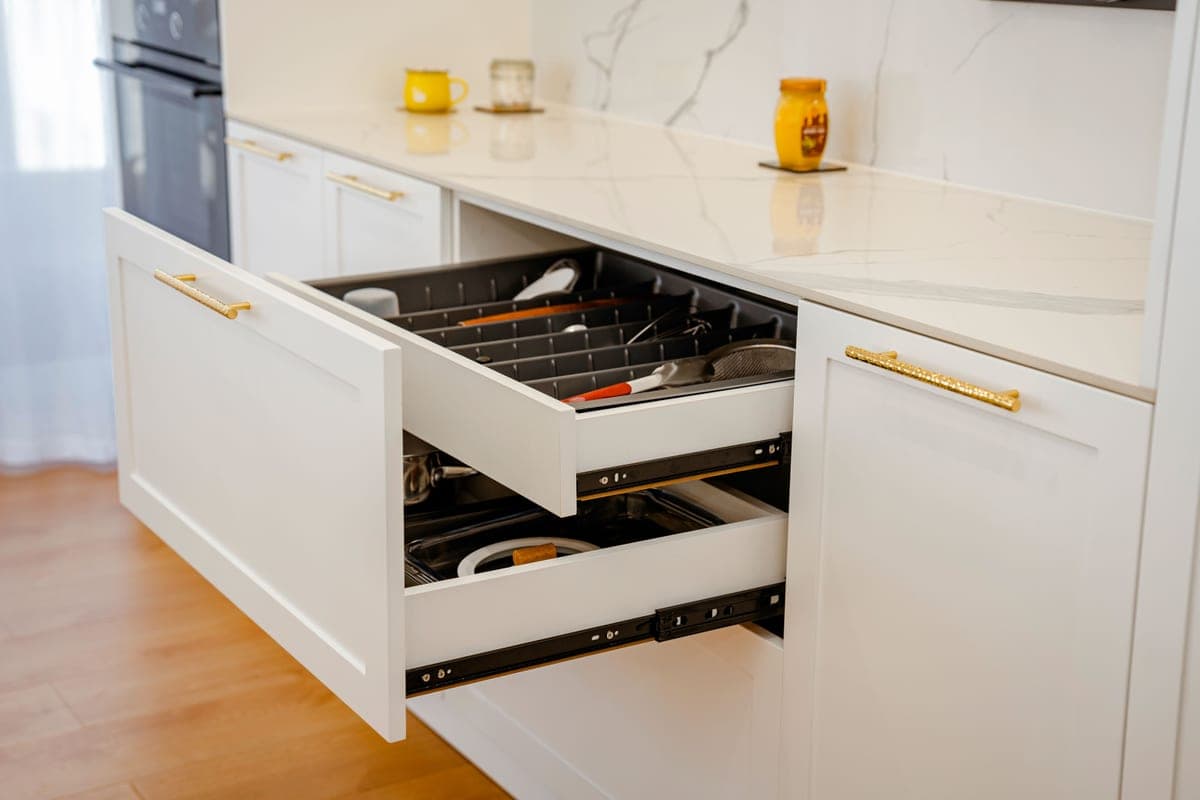 An open drawer in a white fitted kitchen with a marble countertop